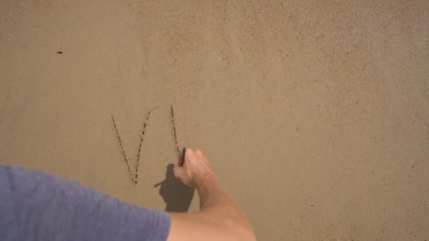 Slowmotion-skott. En man skriver brev VIRUS på sanden på en strand — Stockvideo