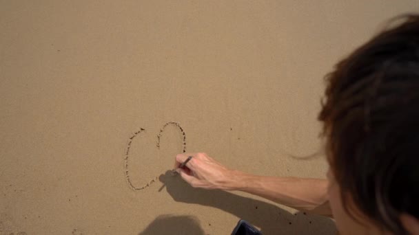 Tir au ralenti. Un homme écrit des lettres COVID-19 sur le sable d'une plage — Video