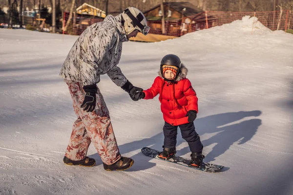 Tata uczy syna snowboardingu. Zajęcia dla dzieci w zimie. Zimowy sport dla dzieci. Styl życia — Zdjęcie stockowe