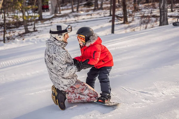 Tata uczy syna snowboardingu. Zajęcia dla dzieci w zimie. Zimowy sport dla dzieci. Styl życia — Zdjęcie stockowe