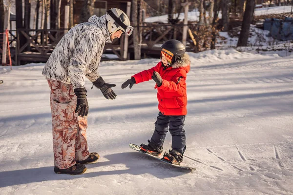 Tata uczy syna snowboardingu. Zajęcia dla dzieci w zimie. Zimowy sport dla dzieci. Styl życia — Zdjęcie stockowe