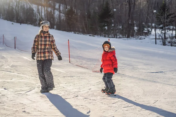 Anya snowboardozni tanítja a fiát. Tevékenységek gyerekeknek télen. Gyermek téli sport. Életmód — Stock Fotó