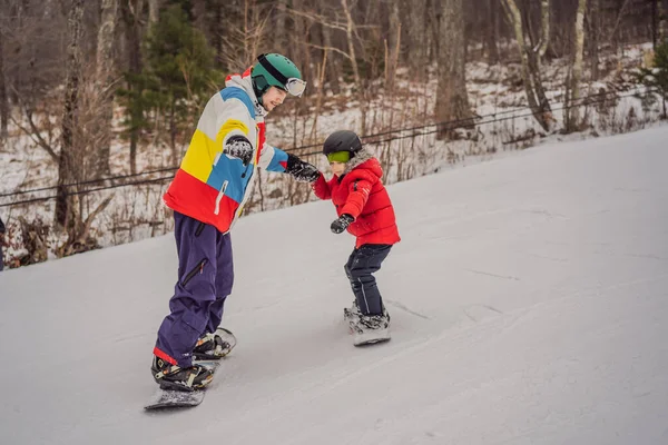 Instruktor snowboardu uczy chłopca jeździć na snowboardzie. Zajęcia dla dzieci w zimie. Zimowy sport dla dzieci. Styl życia — Zdjęcie stockowe