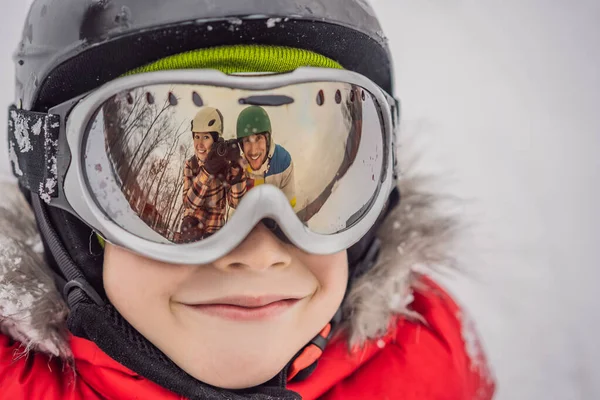 Maman et papa sont reflétés dans les lunettes de ski garçon. Maman et papa enseignent le ski ou le snowboard à un garçon — Photo
