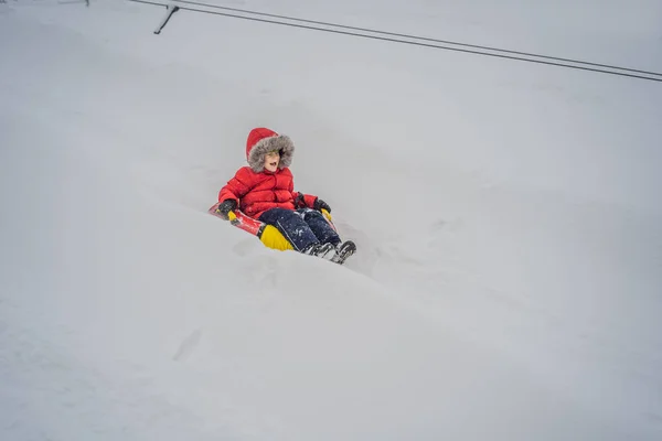 Ребенок веселится на снегоходе. Мальчик ездит на трубе. Зимнее развлечение для детей — стоковое фото