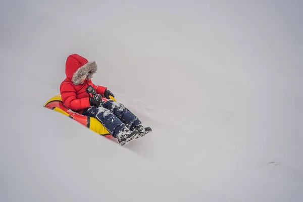 Ребенок веселится на снегоходе. Мальчик ездит на трубе. Зимнее развлечение для детей — стоковое фото