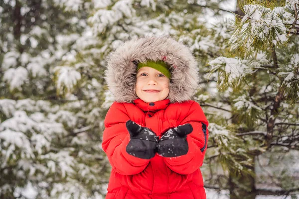 Happy boy plays with snow. Cute kid throwing snow in a winter park. Happy winter holidays. Winter fashion