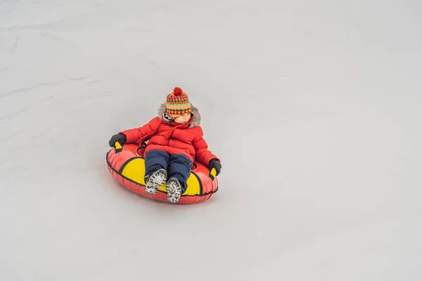 Dítě se baví na sněhové trubici. Ten kluk jezdí na trubkách. Zimní zábava pro děti — Stock fotografie