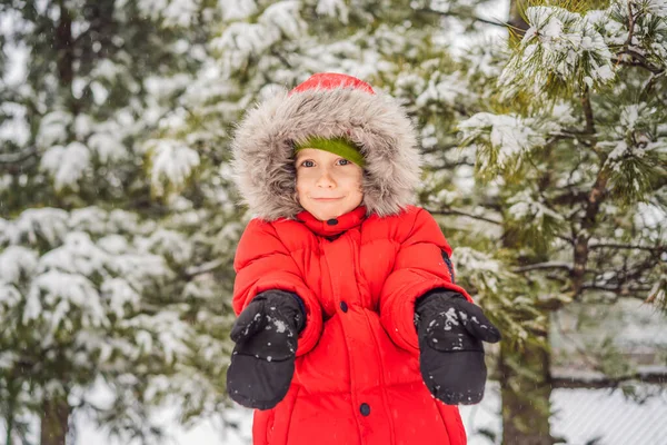 El niño feliz juega con la nieve. Lindo niño lanzando nieve en un parque de invierno. Felices fiestas de invierno. Moda de invierno — Foto de Stock