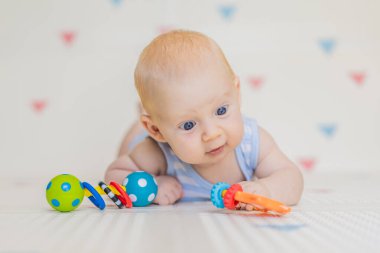 Evdeki yumuşak bir bebek minderinde renkli çıngıraklarla oynayan sevimli bir bebek. Erken gelişim kavramı, duyusal oyun ve bebekler için güvenli öğrenme ortamı.