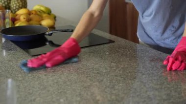 Genç bir adam mutfak masasını temizliyor, evinde temizlik ve düzen sağlıyor. Basit ama önemli bir ev yapımı, bakım ve düzenli ve davetkar bir yer yaratma anı