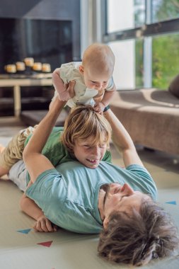 Baba, oğul ve yeni doğan bebek sıcak bir kreşte yerde yatıyorlar ve yeni aile üyelerinin gelişini kutluyorlar. Ebeveynlik, bağlılık ve aile sevgisi kavramı.