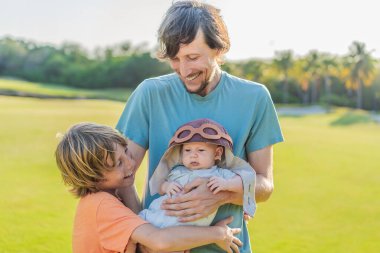 Baba, oğul ve çayır üzerinde yeni doğmuş bir bebek. Pilot şapkası takan bebek havacılık hayallerini sembolize ediyor. Aile bağı kavramı, geleceğin pilotu ve çocukluk arzusu..