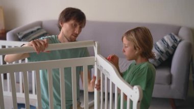 Baba ve oğul yakında doğacak erkek bebek için bir beşik oluşturun. Ebeveynlik kavramı, yeni doğan için hazırlık, aile takım çalışması, bağlanma, sevgi, bakım ve yeni bir hayat beklentisi.