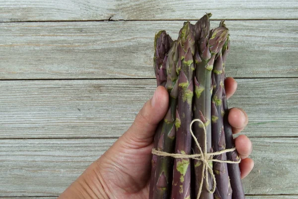 Espárragos Púrpura Manojo Una Mano Sobre Fondo Madera — Foto de Stock