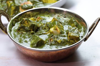 A bowl of Palak Paneer made of Paneer cheese dipped in mildly spiced Spinach gravy on wooden background. clipart