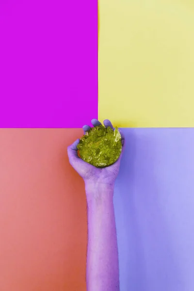 purple hand holding a crystal on a solid colored background.