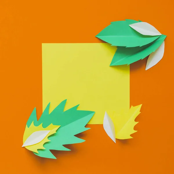 Yellow and green fallen leaves on orange background with frame for text in middle. Minimal and creative.