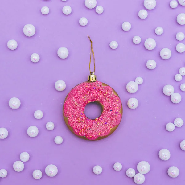 Christmas ball made of pink doughnut among white pearls like snow. Winter holidays concept