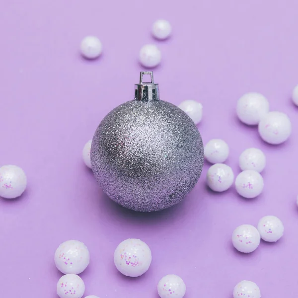 Glitter Christmas ball with white pearls scattered on violet background. Winter decorations.