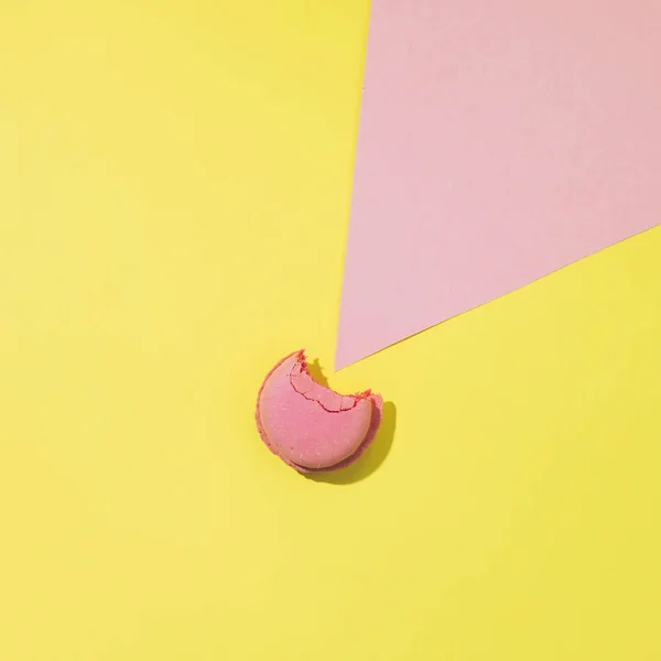 Bitten cake macaron or macaroon on yellow and pink background from above, colorful almond cookies, minimalism, sharp shadow