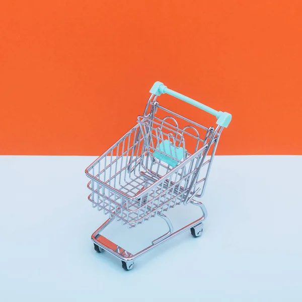 Empty supermarket cart on orange and light blue background
