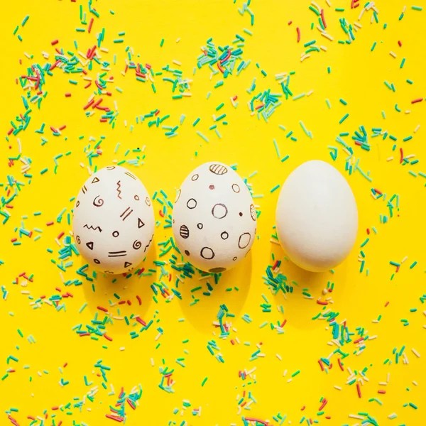 Three Easter eggs with memphis style print on yellow bright background with sprinkled confetti.
