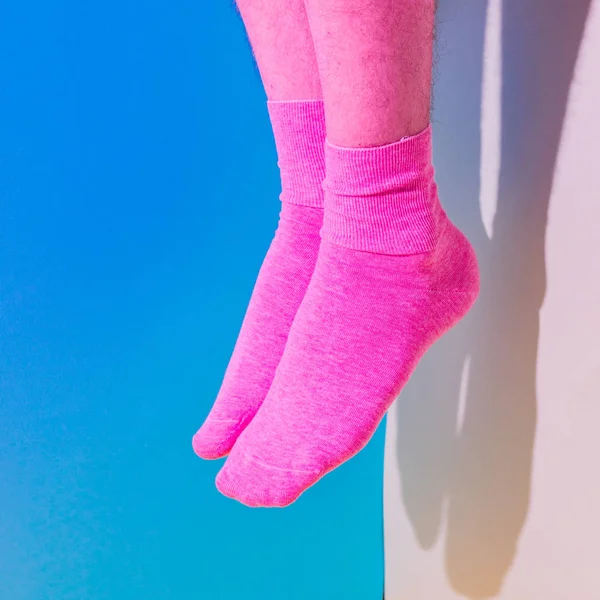 Alien male feet with pink hairy skin in socks flying in the air above bold background in the corner with strong shadows. Duotone colors. Pride concept. Body part