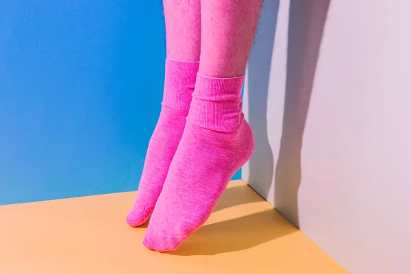 Alien male feet with pink hairy skin in socks flying in the air above bold background in the corner with strong shadows. Duotone colors. Pride concept. Minimalism. Body part