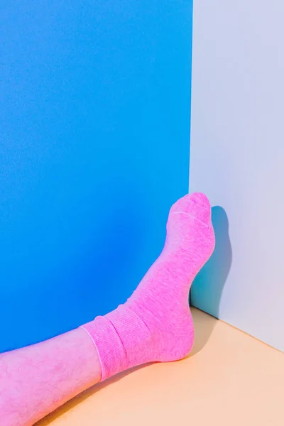 Alien male leg with hairy skin in socks laying on bold background in the corner with strong shadows. Minimal art concept. Body part