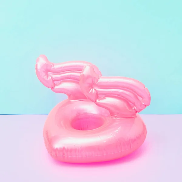 Inflatable pool toy in shape of heart with wings on pastel pink and blue background. Minimalism