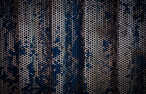 Delikli metal levhanın yakın çekimi altında yumuşak çiçekli kumaş olduğunu gösteriyor. Soyut arka planlar, doku çalışmaları veya endüstriyel tasarım için ideal.