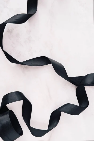 Black ribbon on white marble background layout from above. Copy space for text