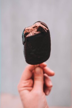 Kadın eli tutarak ısırıldı karanlık çikolatalı dondurma, dondurma. Minimalizm gıda Fotoğrafçılık. Boşaltmak