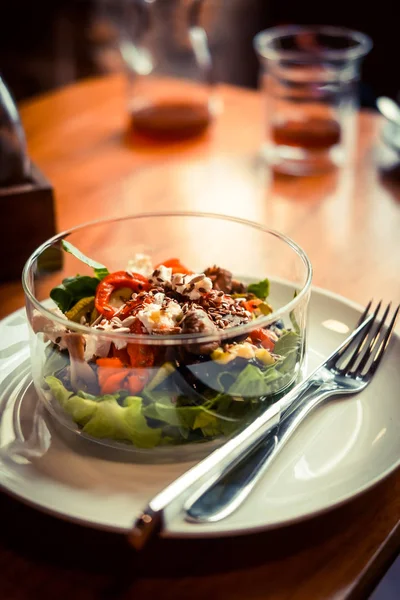 Cam tabak sağlıklı kavrulmuş sebze salatası ahşap bir masa üzerinde. Düşük anahtar gıda fotoğraf, sıcak tonlu filtre