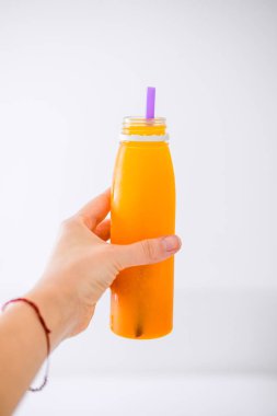 Kadın eli bir şişe soğuk preslenmiş portakal suyu mor saman ile beyaz arka plan üzerinde tutar. Vücut cleance, hızlı, detoks, enerji şarj kavramı. Boşaltmak 