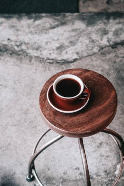 Yukarıdan koyu kahverengi tabakta siyah filtre kahve. Ahşap masa, gri beton zemin, hipster kahve dükkanı. Kopya alanı 