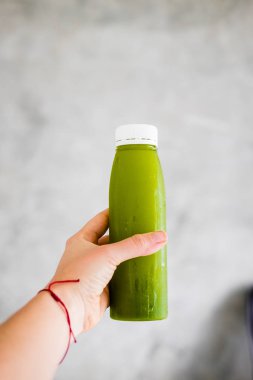 Kadın eli yeşil suyu soğuk preslenmiş bir şişe gri duvara tutar. Vücut cleance, hızlı, detoks kavramı. Minimalizm gıda Fotoğrafçılık. Boşaltmak