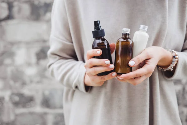 Kadının botles spa kozmetik ile gri duvara tutarak. Güzellik blogger, salon terapisi, Minimalizm kavramı, boşaltmak