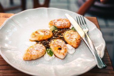 Beyaz tabakta servis edilen süzme peynirli krepler. Tahta masa. Yemek fotoğrafçılığı konsepti