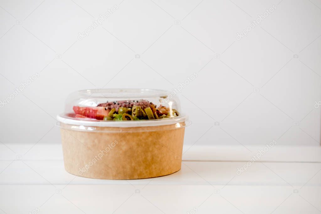 Take away salad in disposable craft paper bowl on white background. Minimalism food photography concept. Mockup, copyspace