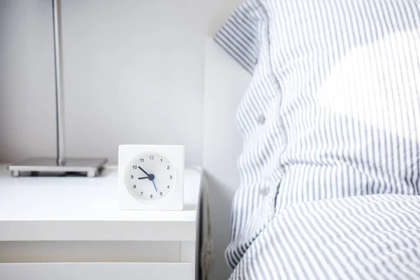 Morning alarm clock in white bedroom interior. Copyspace for text. Minimalist concept