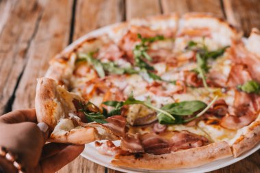 Kadının elini dilim pizza carbonara rustik ahşap masa üzerinde tutun. Gıda fotoğrafçılığı kavramı. Üstten görünüm