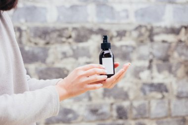 Kadının spa kozmetik kahverengi cam şişe gri duvara tutarak. Güzellik bloglama, salon terapisi, ürün paketi, mockup, Minimalizm kavramı