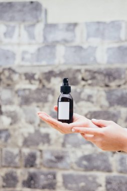 Kadının spa kozmetik kahverengi cam şişe gri duvara tutarak. Güzellik bloglama, salon terapisi, ürün paketi, mockup, Minimalizm kavramı