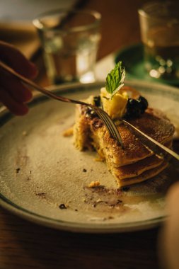 Erkek elleri Amerikan kreplerini bal ve kremayla kesiyor, yukarıdan, ahşap masadan. Ilık renkli görüntü filtresi efekti. Yemek fotoğrafçılığı konsepti