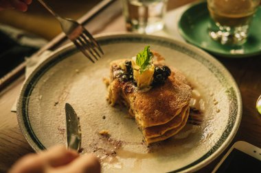 Erkek elleri Amerikan kreplerini bal ve kremayla kesiyor, yukarıdan, ahşap masadan. Ilık renkli görüntü filtresi efekti. Yemek fotoğrafçılığı konsepti