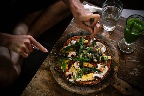 Pria makan pizza vegan mentah di atas meja kayu — Stok Foto