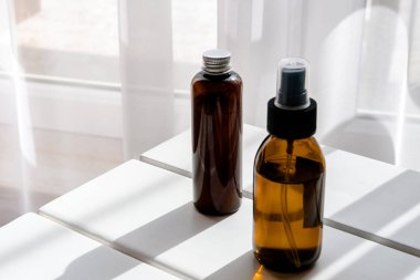 Beyaz masa üzerinde organik kozmetik ürünleri olan plastik ve cam kahverengi şişeler. Direkt ışık. Güzellik blog minimalizmi kavramı