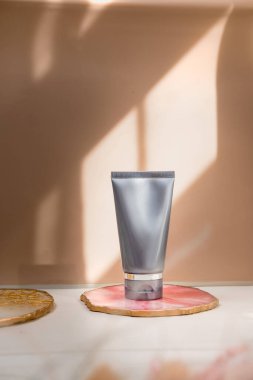 Işık nötr pastel arka planda gri kozmetik tüp, ışıklar ve gölgeler. Doğal minimalizm, temiz. Minimal natürmort. Güzellik günlüğü, markalaşma düzeni, cilt bakımı maketi, boşluk kopyalama